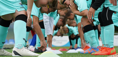 Spielende Kinder in der Fußballschule tragen türkise Trikotsets und greifen nach Hütchen, die auf dem Rasen liegen.